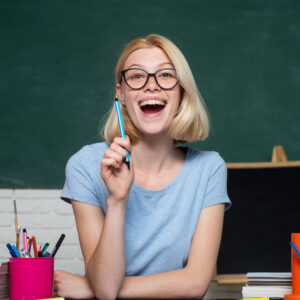 Portrait of a female student in university. Student and tutoring education concept. Funny female young teacher in the classroom. Young teacher in glasses over green chalkboard background
